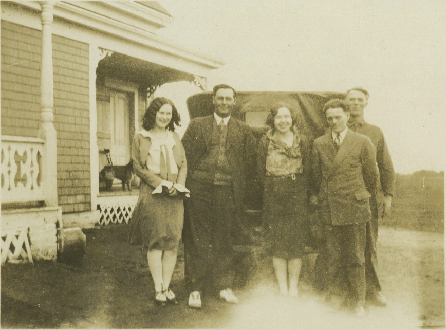 Five people outside a house beside a car