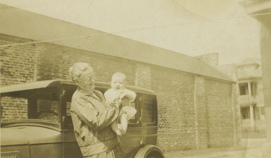 Unidentified adult holding a baby beside a car