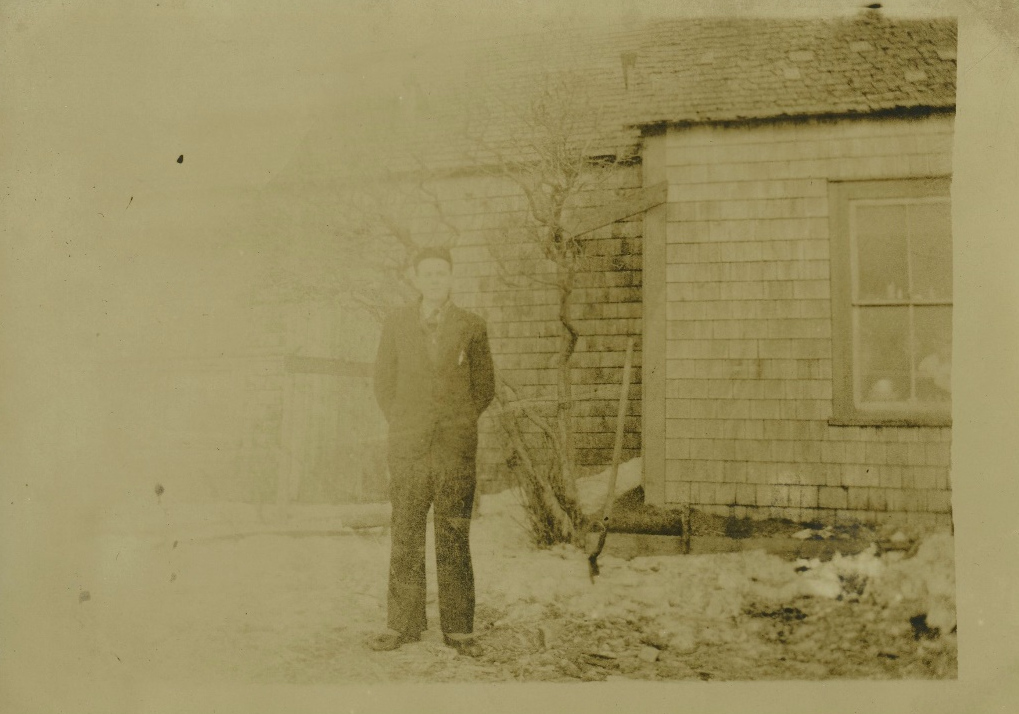 Unidentified man outside a shingled building